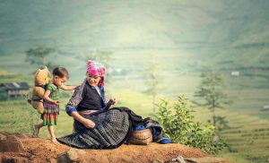 Eine Mutter sitzt zusammen mit ihrem Kind auf einem Berg und macht Pause von der Feldarbeit.